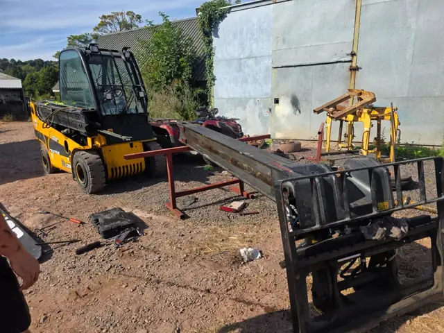 JCB telehandler with its boom laid out on stands for repair in a yard