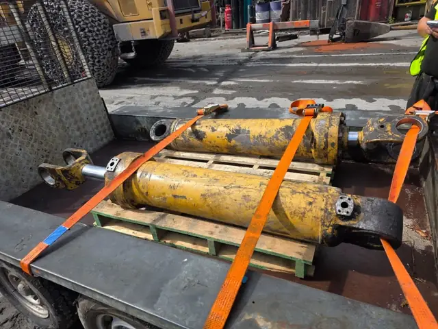 Two yellow hydraulic rams strapped down on a trailer