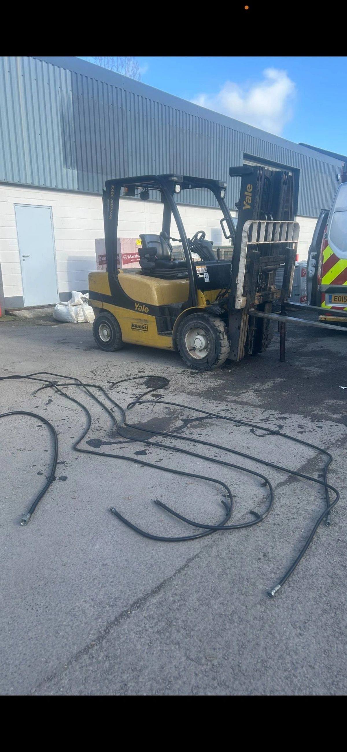 Forklift in a yard with old hydraulic hoses laid out on the ground
